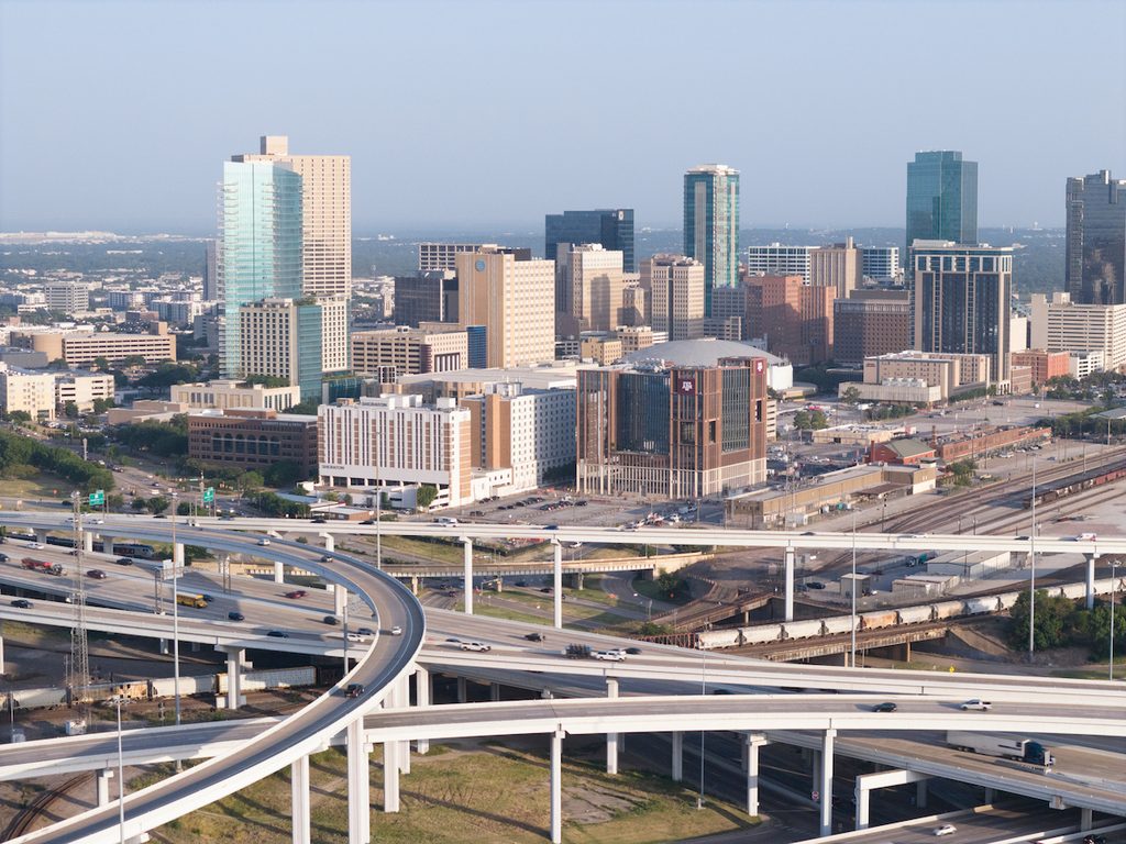 A bustling urban skyline with modern skyscrapers overlooks a complex network of elevated highways and overpasses.